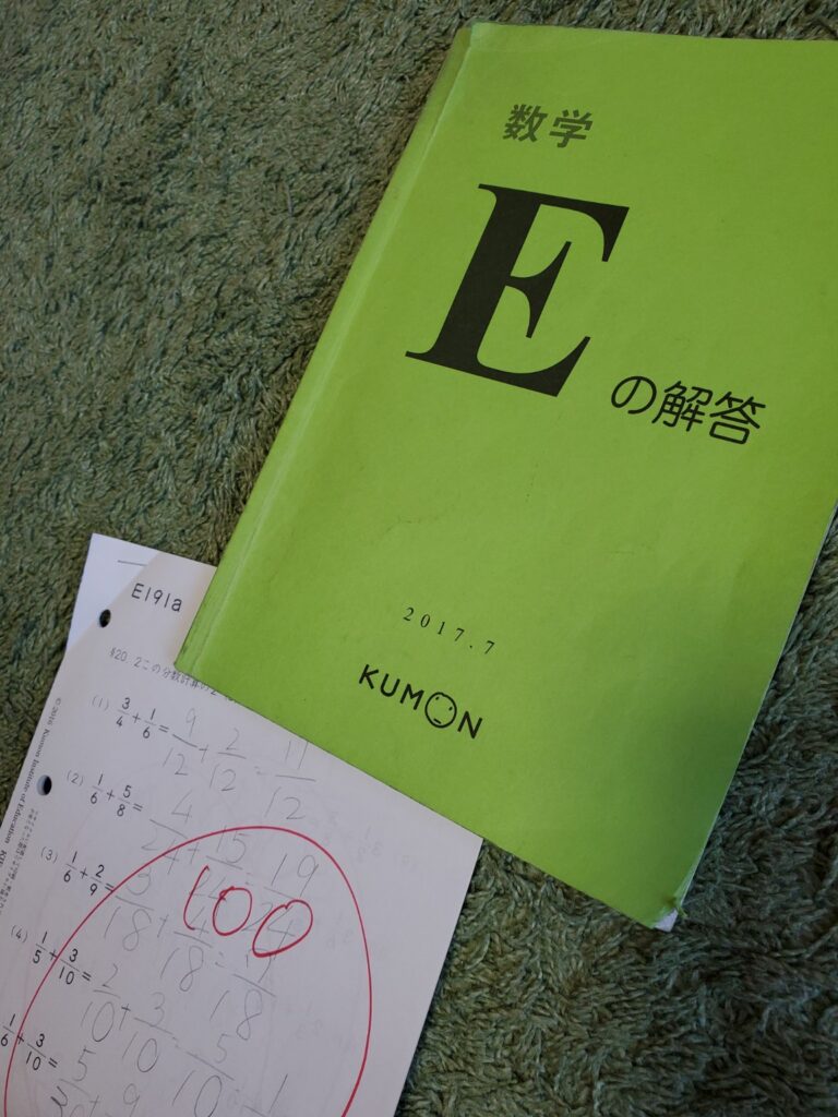 公文数学E教材の解答集と、100点がついた家庭学習プリントが並んでいる写真